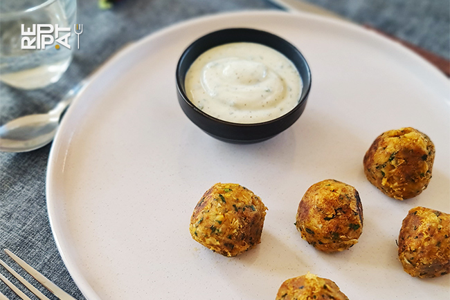 Boulettes de pois chiches aux épices posées sur une assiette blanche et un ramequin d'une sauce blanche