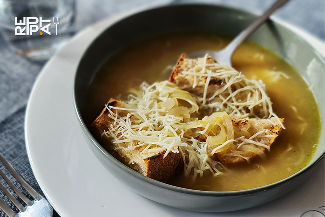 Soupe avec du pain et du gruyère râpé dans une assiette creuse de couleur marron