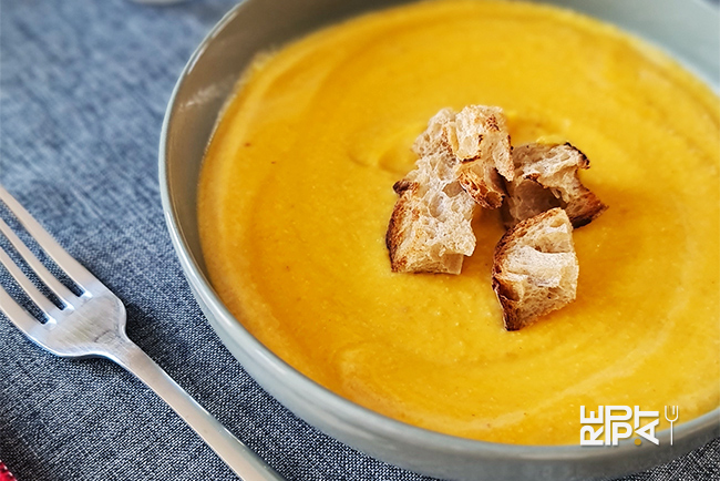 Soupe jaune épaisse avec des croûtons de pain grillés dans une assiette creuse grise sur une nappe gris foncé